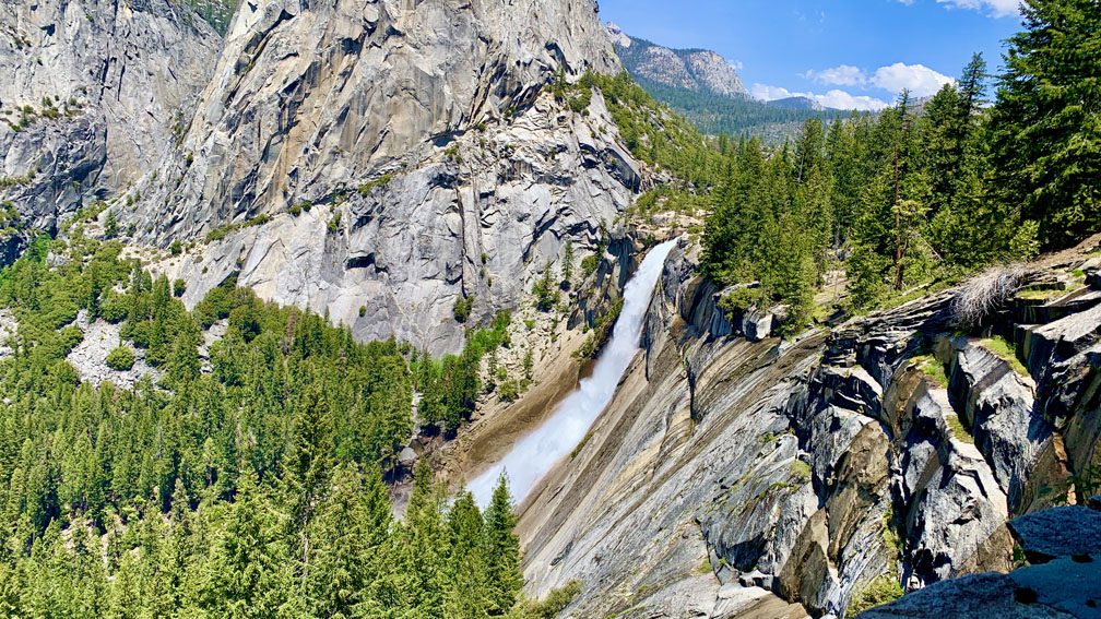 Nevada Fall in Yosemite National Park from a distance running down the granite rock with forest trees in the fore and background.
