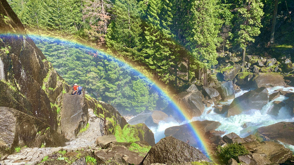 A rainbow created by the mist from Vernal Falls is over a hiker on the trail to the top of Vernal Falls.