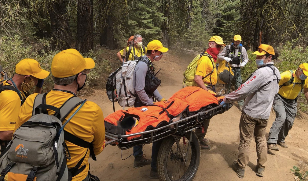 Search and Rescue personnel remove an injured hiker from the wilderness on a wheeled gurney.