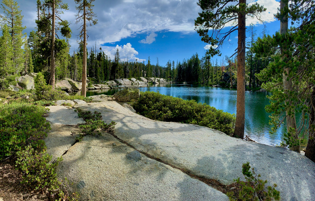 Granite rock sets before a pond on the Sterling Lake Trail with forest in the background.