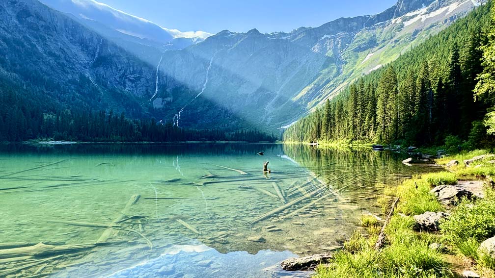 A view of Avalanche Lake at Glacier National Park with forest trees, mountains, and waterfalls in the background.
