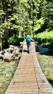 A hiker crosses the plank suspension bridge to Grinnell Lake.