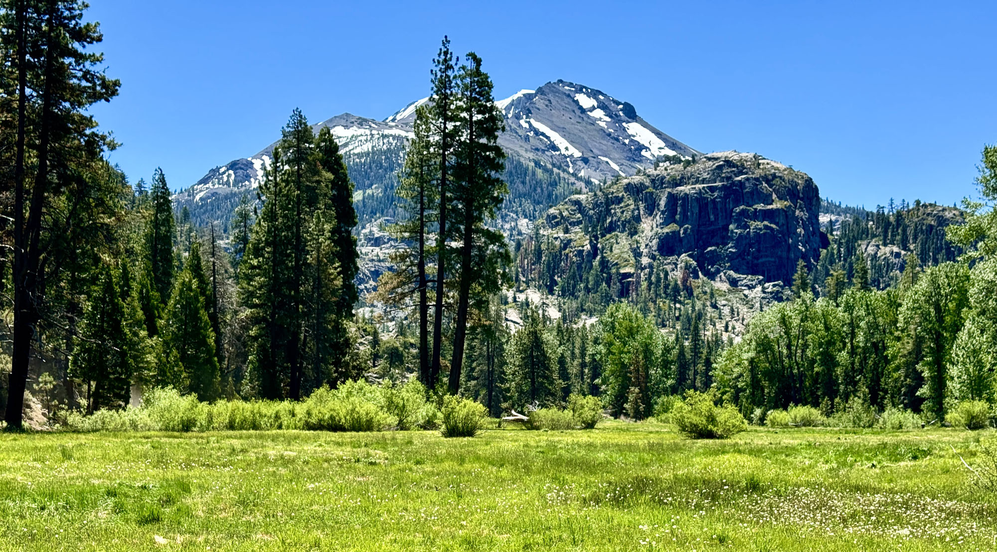 A mountain sits in the background of a green meadow on the trail to Relief Reservoir.
