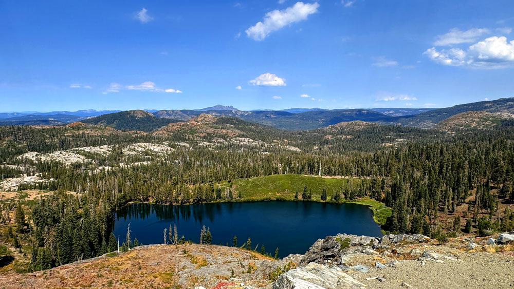 Milk Lake sits below a ledge with the Sierra Buttes in the distant background.